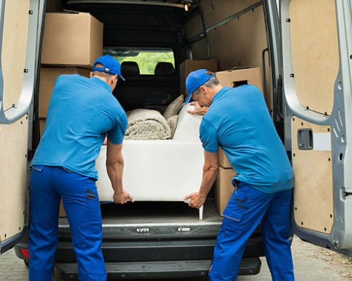 Two Male Workers In Blue Uniform Adjusting Sofa In Truck
